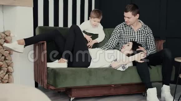 一个怀孕的妻子躺在她丈夫的大腿上在一个家庭氛围中他们的四岁儿子视频的预览图