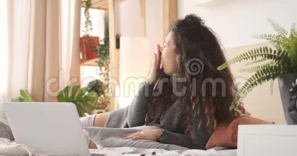 疲惫的女人在床上用笔记本电脑视频的预览图