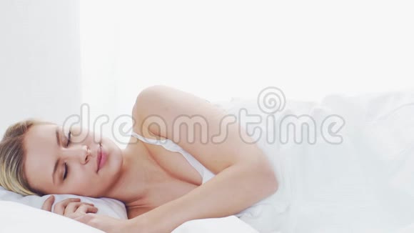 躺在床上的年轻女子美丽的金发女郎早上在卧室健康和休息的理念视频的预览图