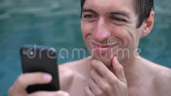 在游泳池里用智能手机为正在度假的微笑青年做特写视频的预览图