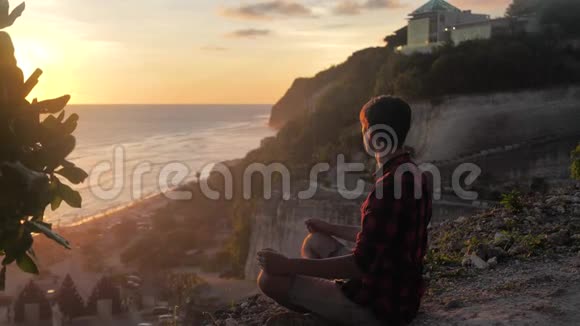 人们坐在岩石上对着美丽的日落沉思视频的预览图