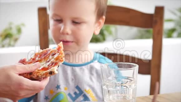 妈妈给她儿子一片披萨快乐的孩子急切地在餐馆里吃意大利披萨儿童健康视频的预览图