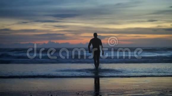 英俊的肌肉男在夕阳下走向海浪的剪影视频的预览图