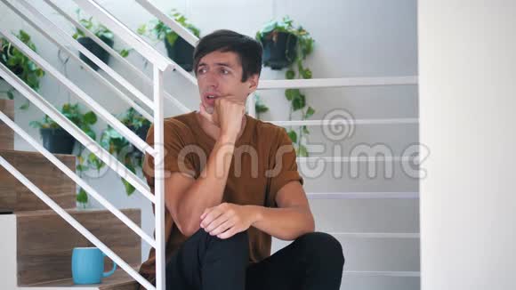 痛苦悲伤和沮丧的年轻人独自坐在家里的楼梯上痛苦悲伤的人视频的预览图