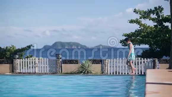 小女孩正在海边和山丘背景的热带酒店的游泳池附近散步视频的预览图