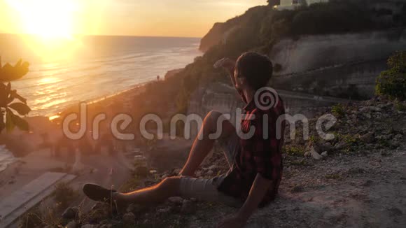 人类旅行者坐在岩石上欣赏日落的海景徒步旅行者坐在大石头上放松并欣赏风景视频的预览图
