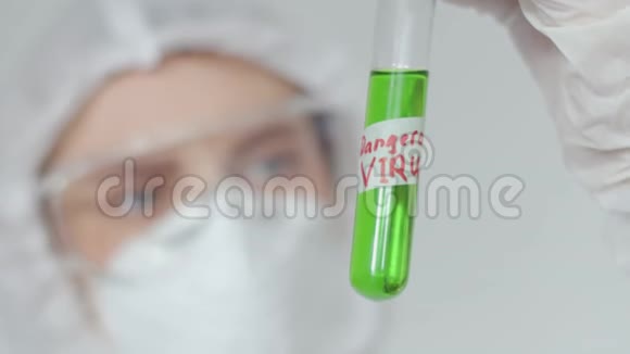 一个戴防护眼镜和医用口罩的女孩检查一个装有绿色液体标记的危险病毒的试管视频的预览图