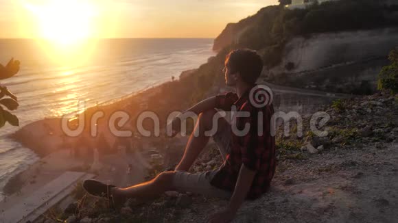 人类旅行者坐在岩石上欣赏日落的海景徒步旅行者坐在大石头上放松并欣赏风景视频的预览图