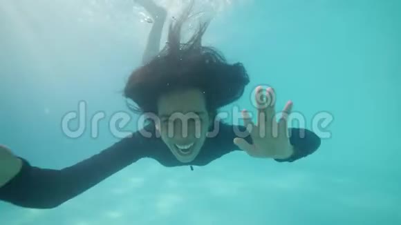 快乐的亚洲女孩看着相机在水下微笑在游泳池里挥动双手视频的预览图