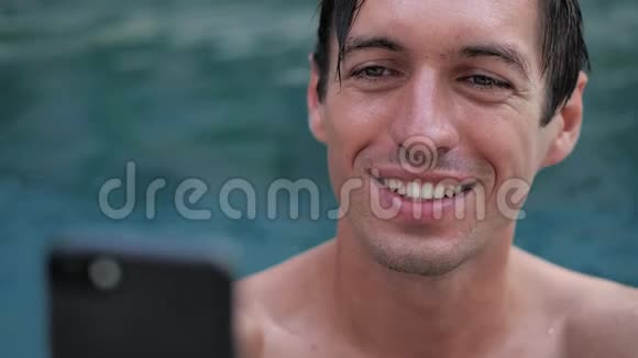 在游泳池里用智能手机为正在度假的微笑青年做特写视频的预览图