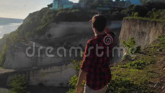 年轻的男性旅行者站在海边的岩石上欣赏美丽的日落视频的预览图