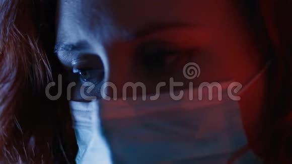 一边看着体贴悲伤的女人戴着外科面具眼睛闭着蓝色和红色的光病毒流行视频的预览图