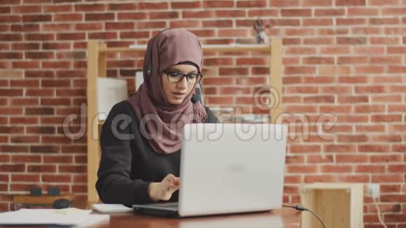 一个戴头巾的穆斯林学生在呼叫中心工作一个年轻的女孩做一个操作员并帮助处理订单视频的预览图