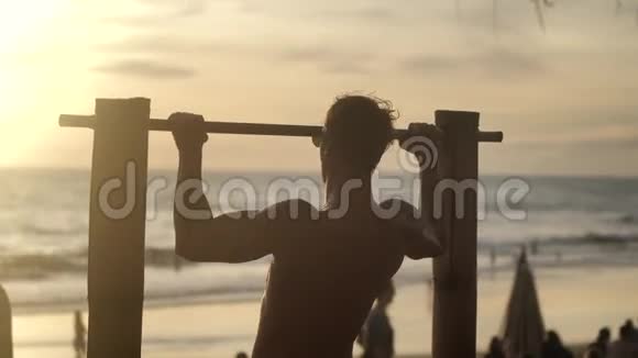 在日落的背景下年轻的肌肉男在海滩上的水平杆上做拉力运动视频的预览图