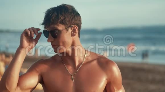日落时分英俊的肌肉男在海滩上戴上太阳镜的肖像视频的预览图