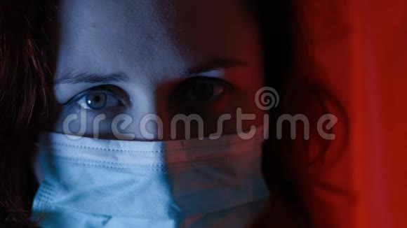 体贴悲伤的女人眼睛闭上戴着手术面具看着远处冠状病毒大流行视频的预览图
