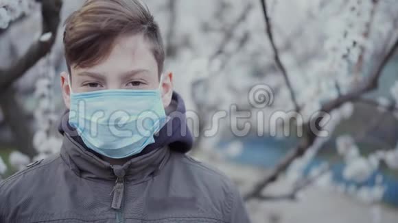 一个戴着医学面具的少年在一棵盛开的树的背景上视频的预览图