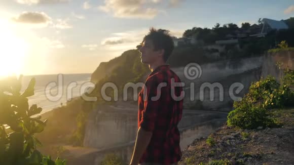 年轻的男性旅行者站在海边的岩石上欣赏美丽的日落视频的预览图