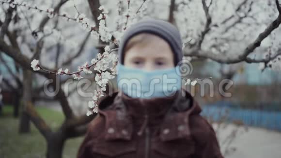 一个5岁的孩子戴着医学面具在一棵开花的树的背景上视频的预览图