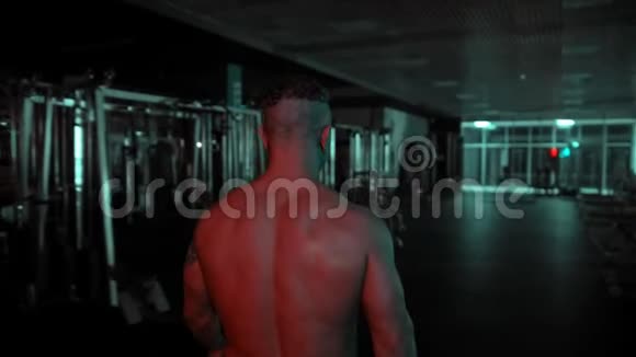 一个穿着无衫的成年健美运动员在黑暗的健身房里行走里面有霓虹灯视频的预览图