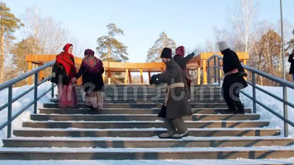 俄罗斯民间穿着毡靴的男女正在冬季公园的楼梯上跳舞视频的预览图