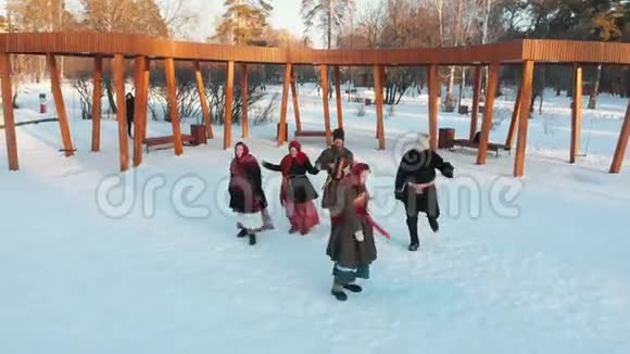 俄罗斯民俗穿着服装的快乐的俄罗斯人正在雪地公园跳舞视频的预览图