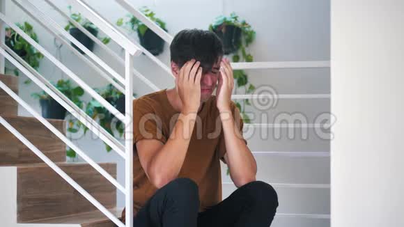 痛苦悲伤和沮丧的年轻人独自坐在家里的楼梯上痛苦悲伤的人视频的预览图