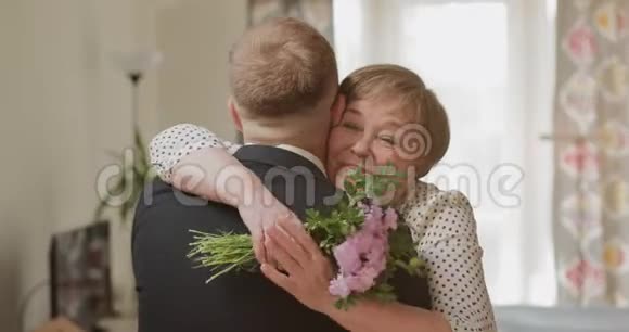快乐漂亮成熟的母亲拥抱她的成年儿子同时手里拿着花他去看望退休的人视频的预览图