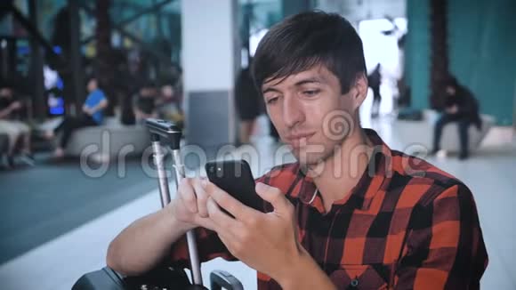在机场候机楼穿着格子衬衫带行李的游客使用智能手机等待登机视频的预览图