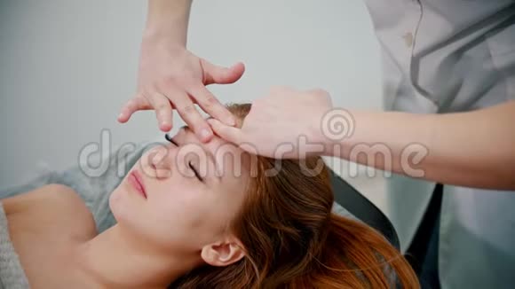 按摩女性按摩师用手按摩红发妇女的脸视频的预览图