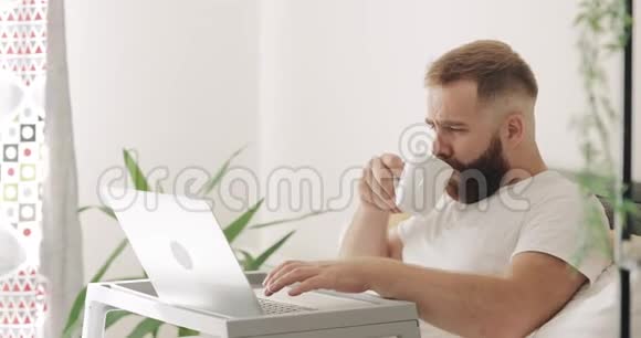 侧观英俊集中男子打字时躺在床上的早晨三十岁的小胡子在家工作视频的预览图