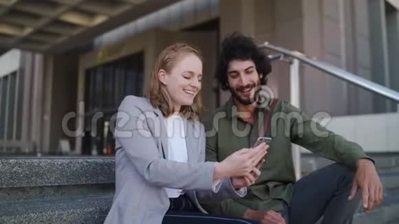 一位穿着商务服的漂亮女人展示了一位英俊的男人她的智能手机坐在一起办公视频的预览图