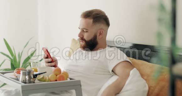 侧视留胡子的家伙在他的智能手机上打字信息而坐在食物托盘在早上帅哥进来了视频的预览图
