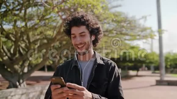 一个快乐的年轻人在公园里散步时用手机听音乐的肖像一个快乐的人在公园里视频的预览图