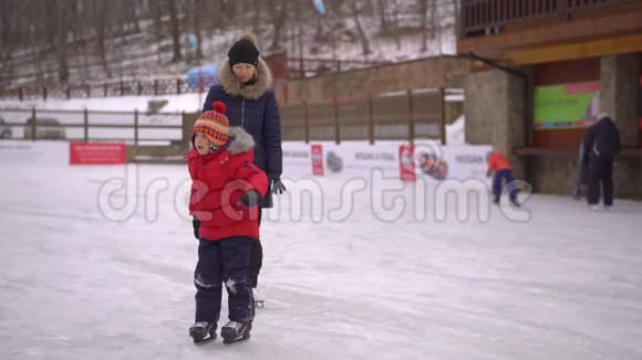年轻的妈妈和一个小男孩在溜冰场上小男孩学会滑冰冬季活动概念视频的预览图