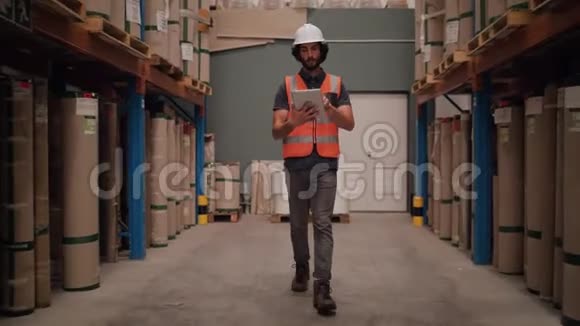 一名年轻的男性工人在堆满货物的大仓库里用数字平板电脑维护记录视频的预览图