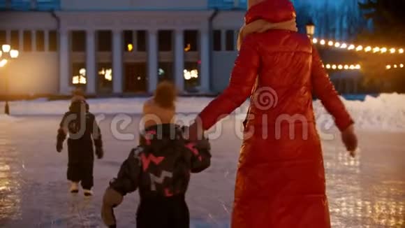 一家人的母亲和两个孩子晚上在明亮的灯光下在公共冰场上滑冰后景视频的预览图
