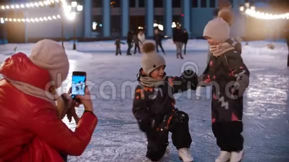 两个小孩在溜冰场上跳舞他们的母亲用电话摄影机拍摄他们视频的预览图