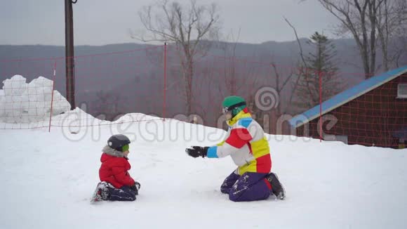 一个年轻人和他的小儿子在一个山区度假活动公园的滑雪坡上玩得很开心寒假概念视频的预览图
