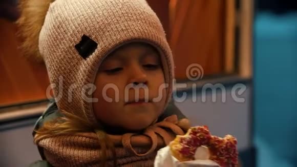 一个穿着冬装在户外吃甜甜圈的小女孩视频的预览图