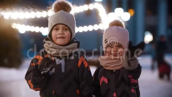 两个小孩站在公共冰场上用手在镜头里挥舞着视频的预览图