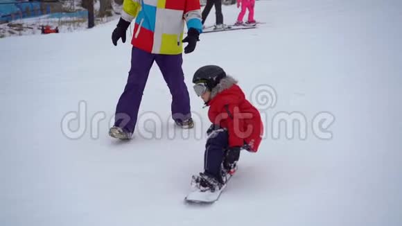 年轻人滑雪板教练教小男孩如何骑滑雪板冬季活动概念慢镜头视频的预览图