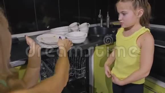 妈妈教女儿聪明的女孩学习使用洗碗机年轻的女主人孩子们在装脏盘子视频的预览图