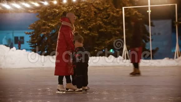 一家年轻的母亲和两个孩子牵着手在溜冰场上滑冰视频的预览图