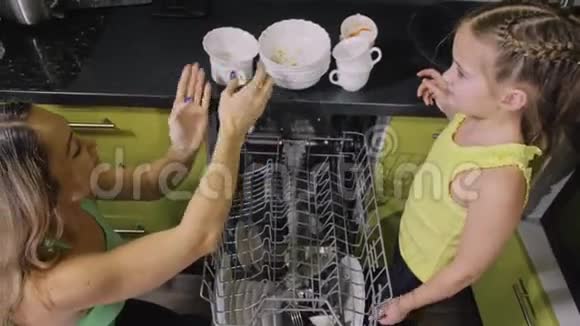 妈妈教女儿聪明的女孩学习使用洗碗机年轻的女主人孩子们在装脏盘子视频的预览图
