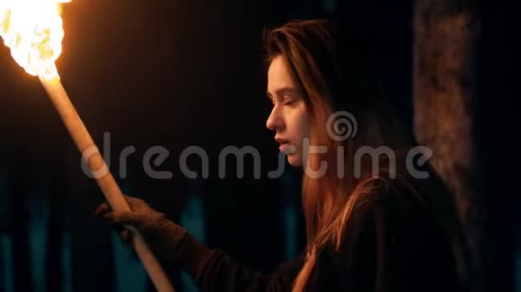 年轻女子站在森林里手里拿着一把火把在森林里走开视频的预览图