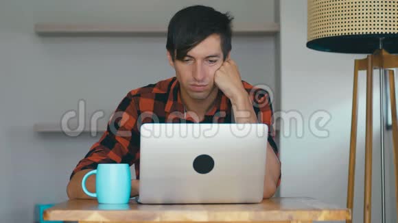 年轻的商人坐在家里的办公桌前用笔记本电脑自由职业者在家里和视频的预览图