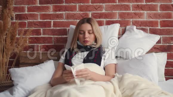 一个年轻的女人躺在铺着毯子的床上咳嗽着用手帕捂住嘴然后穿上了医疗用品视频的预览图