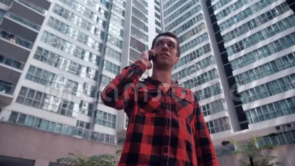 有智能手机的年轻人站在城市的户外打电话背景上的摩天大楼视频的预览图