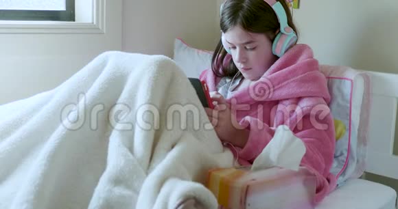 一个躺在床上看着平板电脑的小女孩戴着耳机穿着一件长袍视频的预览图